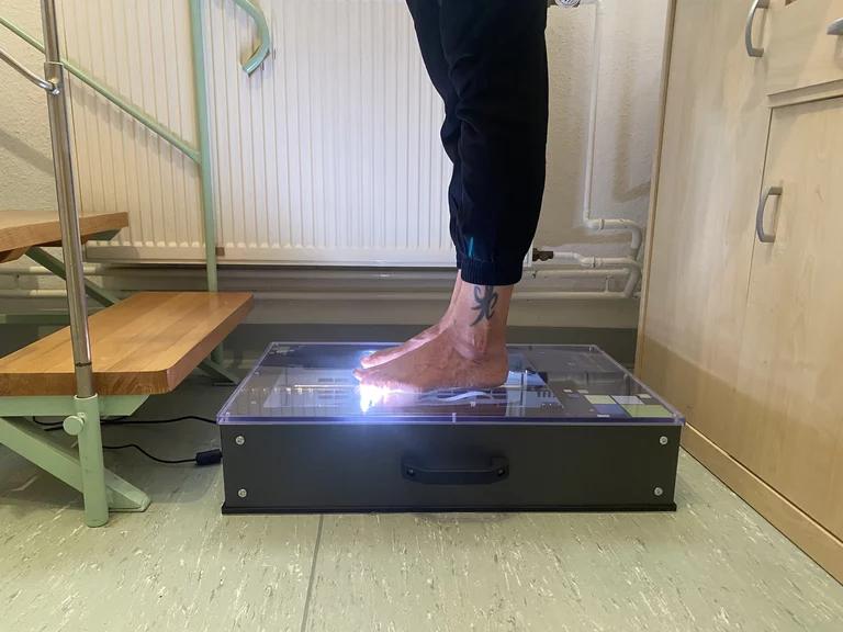 Eine Person steht auf einem Messscanner; sichtbar sind die Füße während der Messung.